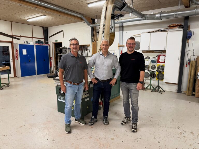 Tre mænd fra Pribo og Tømrermester Per Rasmussens Eftf. står sammen på et tømrerværksted