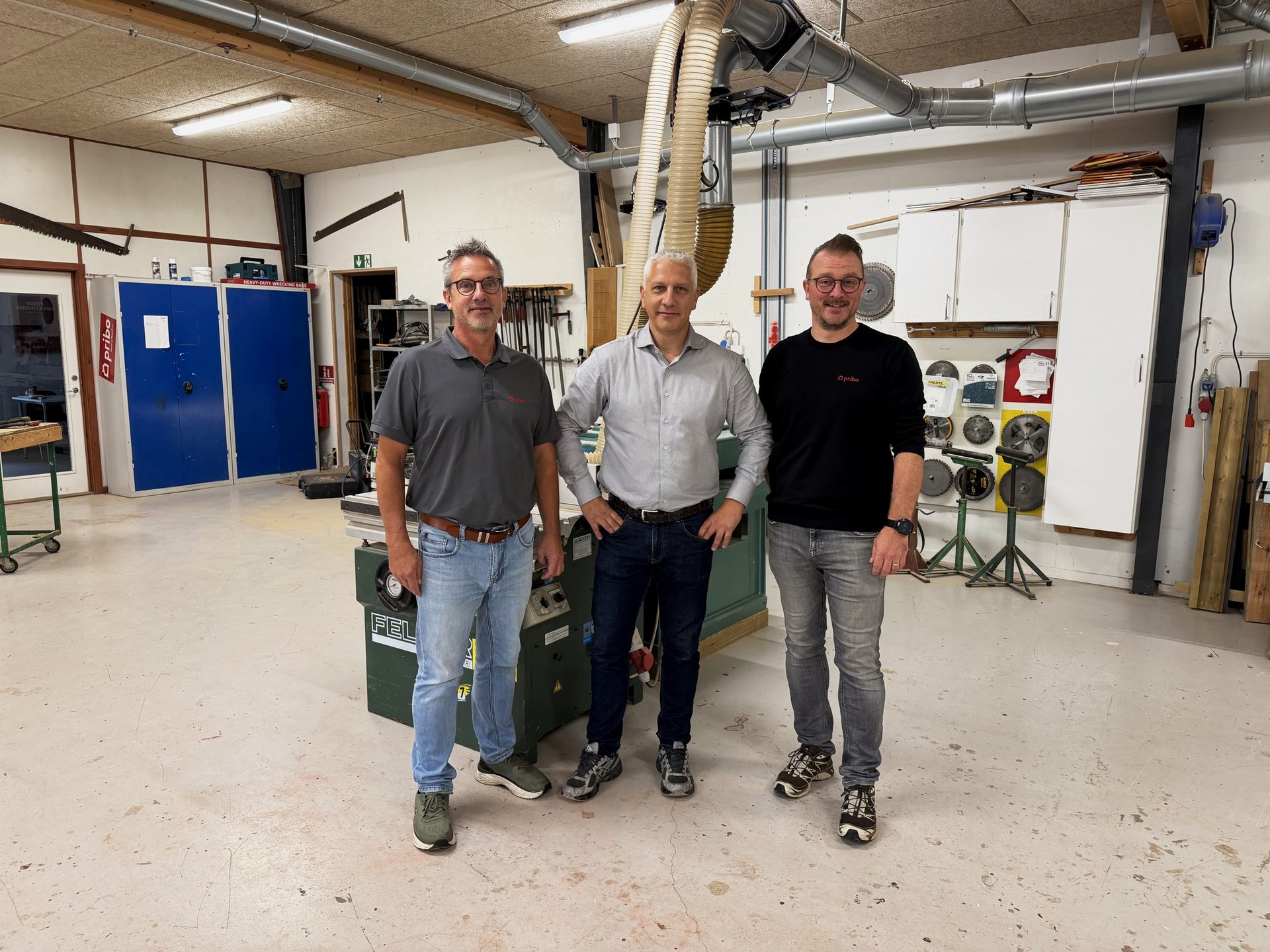 Tre mænd fra Pribo og Tømrermester Per Rasmussens Eftf. står sammen på et tømrerværksted